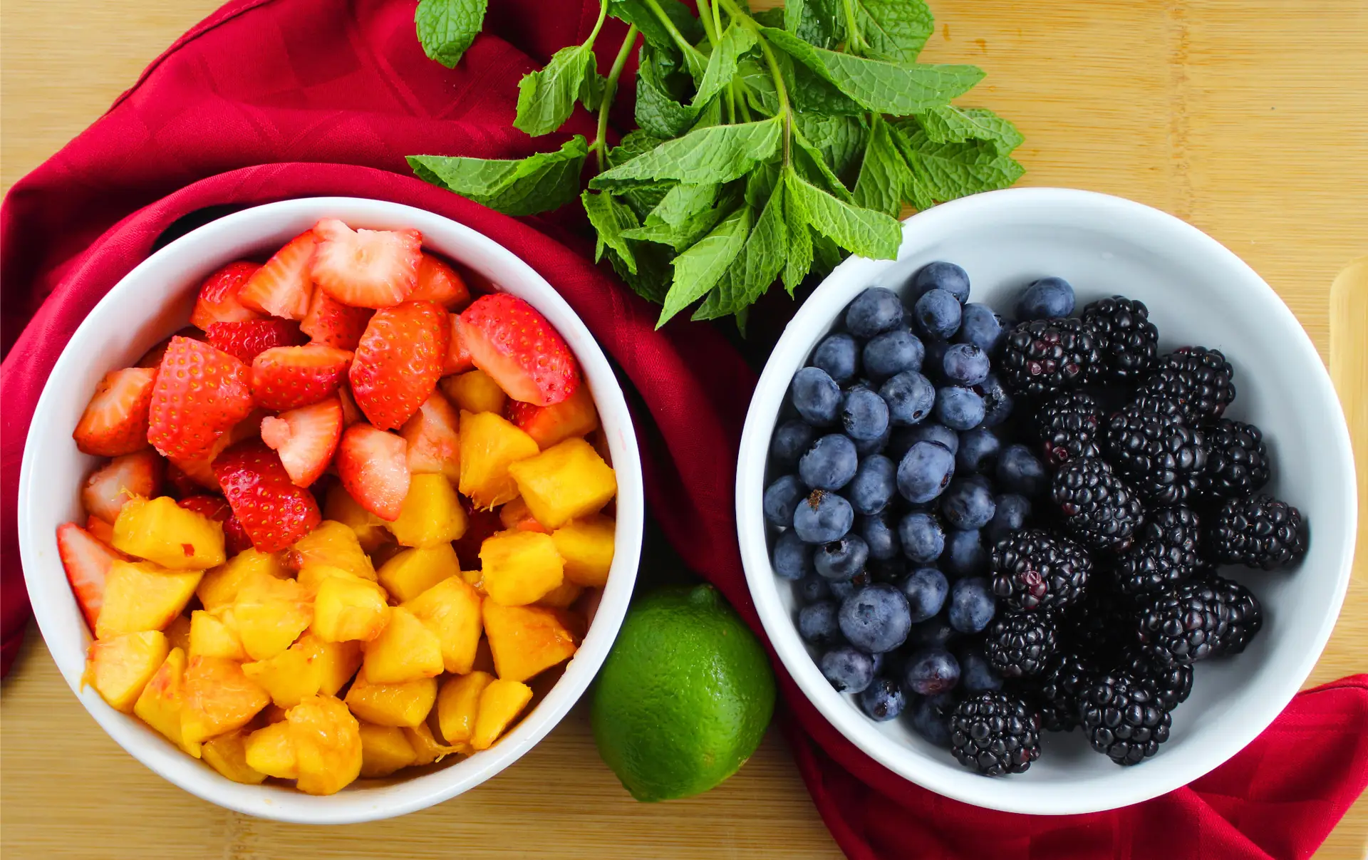 Two bowls of fresh summertime fruit prepped for making paleo fruit soup. Fresh mint leaves and lime.