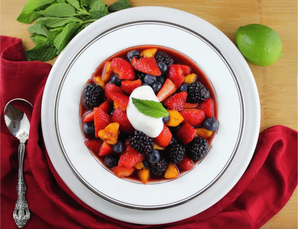 Bowl of paleo summertime fruit soup topped with non-dairy coconut yogurt and fresh mint leaf