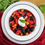 Bowl of paleo summertime fruit soup topped with non-dairy coconut yogurt and fresh mint leaf