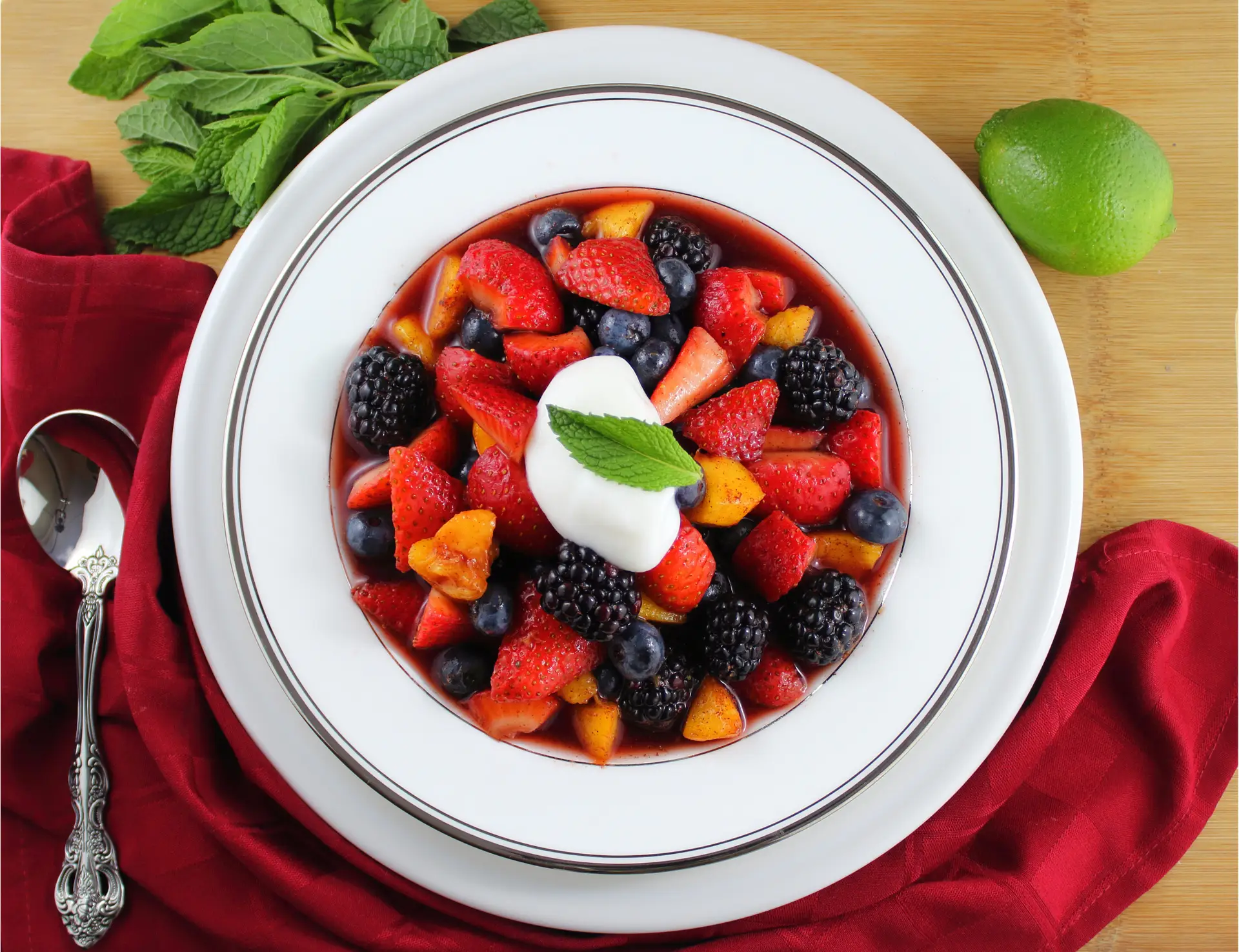 Bowl of paleo summertime fruit soup topped with non-dairy coconut yogurt and fresh mint leaf