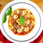Bowl of Italian Sausage Tortellini Soup with fresh basil leaves garnish